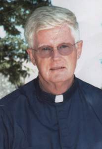 Patrick Samway, a priest in a blue shirt, standing in front of a tree.