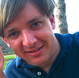 Tad Bartlett, wearing a blue shirt, is holding a cell phone.