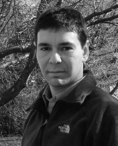 A black and white photo of a man in front of trees.