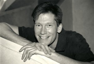 A black and white photo of a smiling man leaning on a railing.