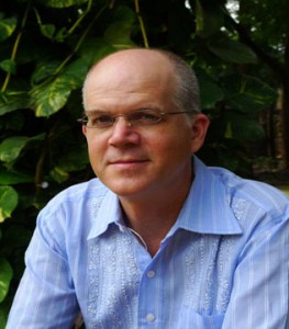 A bald man in a blue shirt sitting on a bench.