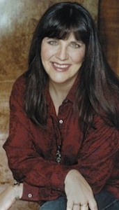 A woman in a red shirt is sitting on a wooden floor.