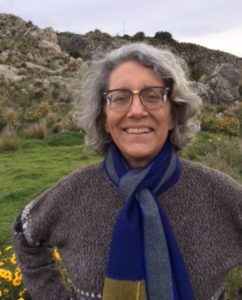 A woman wearing glasses and a blue scarf standing in a grassy field.