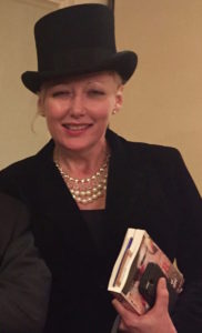 A woman in a top hat holding a book.