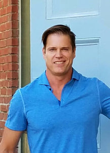 A man in a blue shirt standing in front of a blue door.