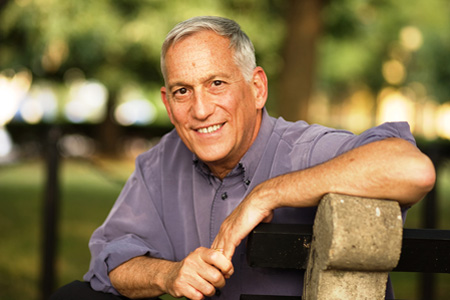 An older man leaning on a bench in a park.