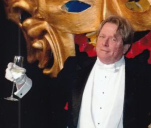 A man in a tuxedo holding a glass of wine.