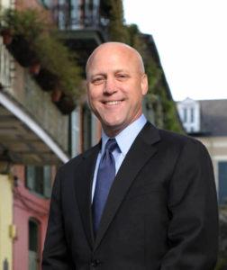 A bald man in a suit standing in front of a building.