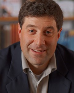 A man smiling in front of a bookshelf.