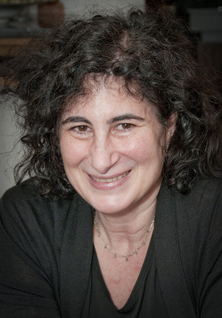 Woman with curly hair smiling and wearing a necklace.